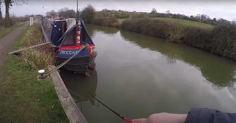 lure fishing on a canal for pike by a moored boat